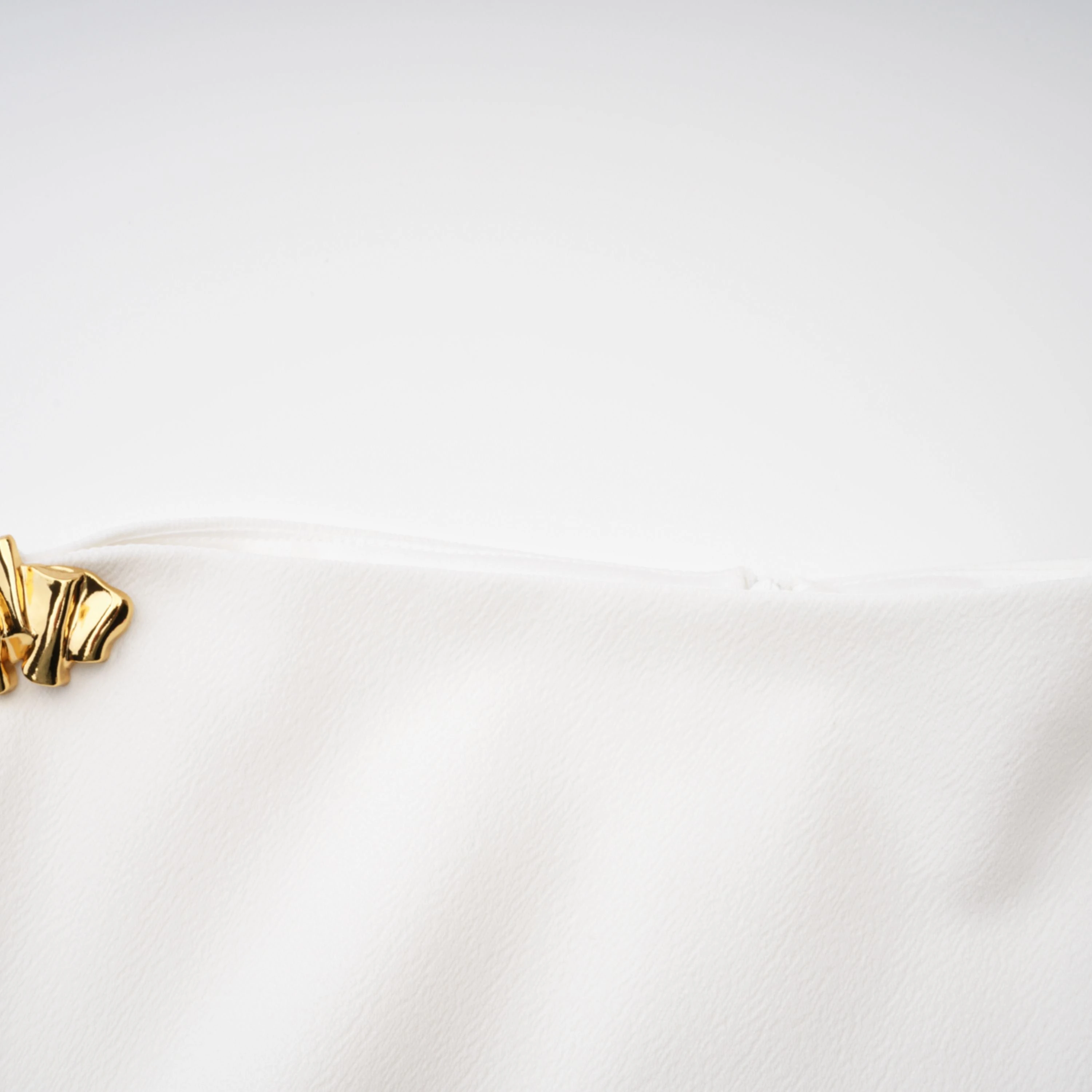 White sleeveless midi dress featuring a high drape neck with a brooch detail and a structured asymmetric handkerchief skirt