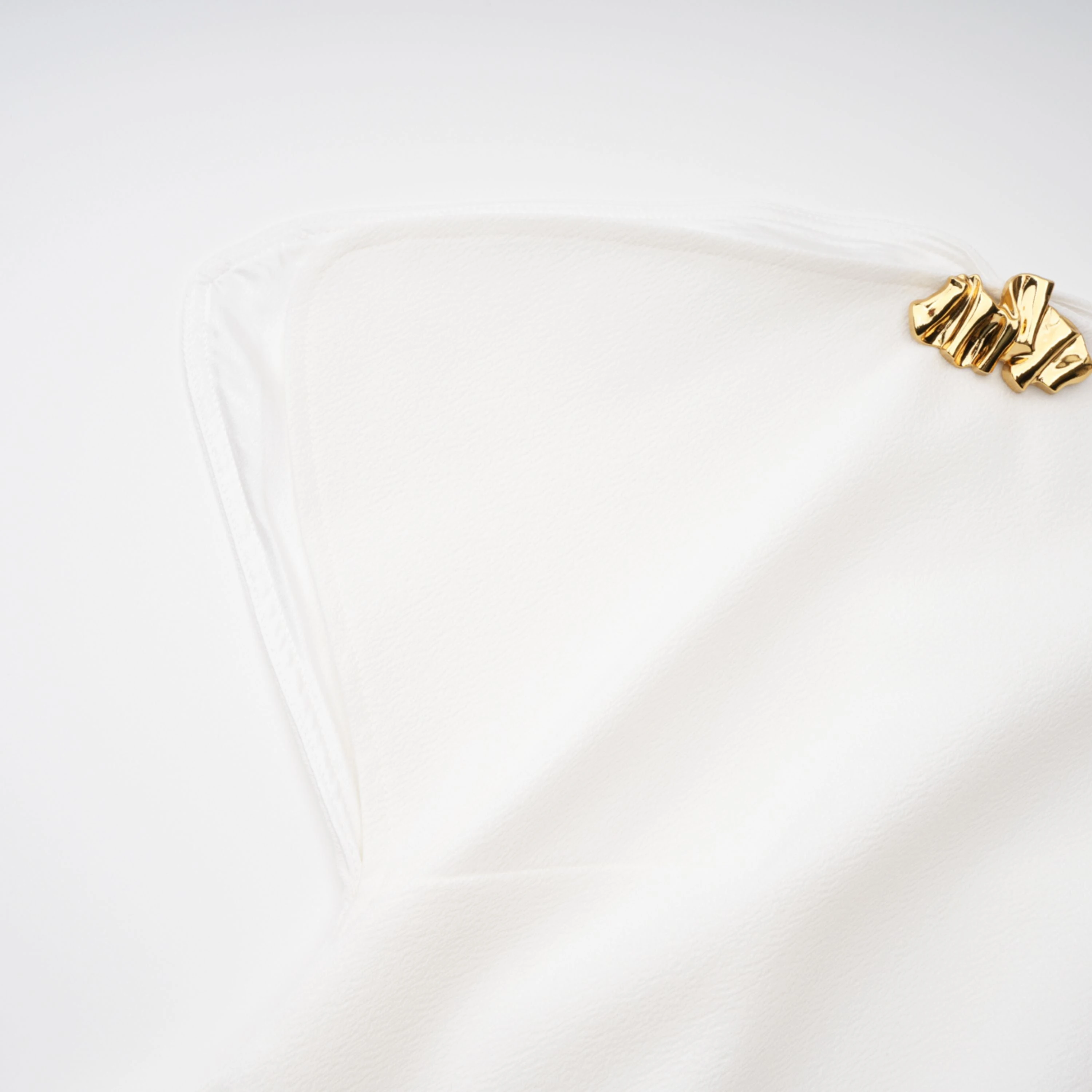 White sleeveless midi dress featuring a high drape neck with a brooch detail and a structured asymmetric handkerchief skirt